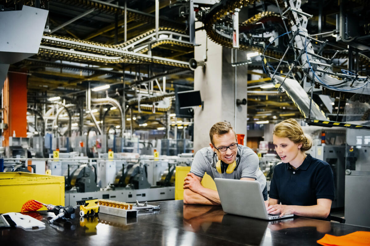 zwei jüngere Ingenieure arbeiten am Laptop in der Verpackungsstraße einer großen Druckerei
 © Tom Werner/ Getty Images