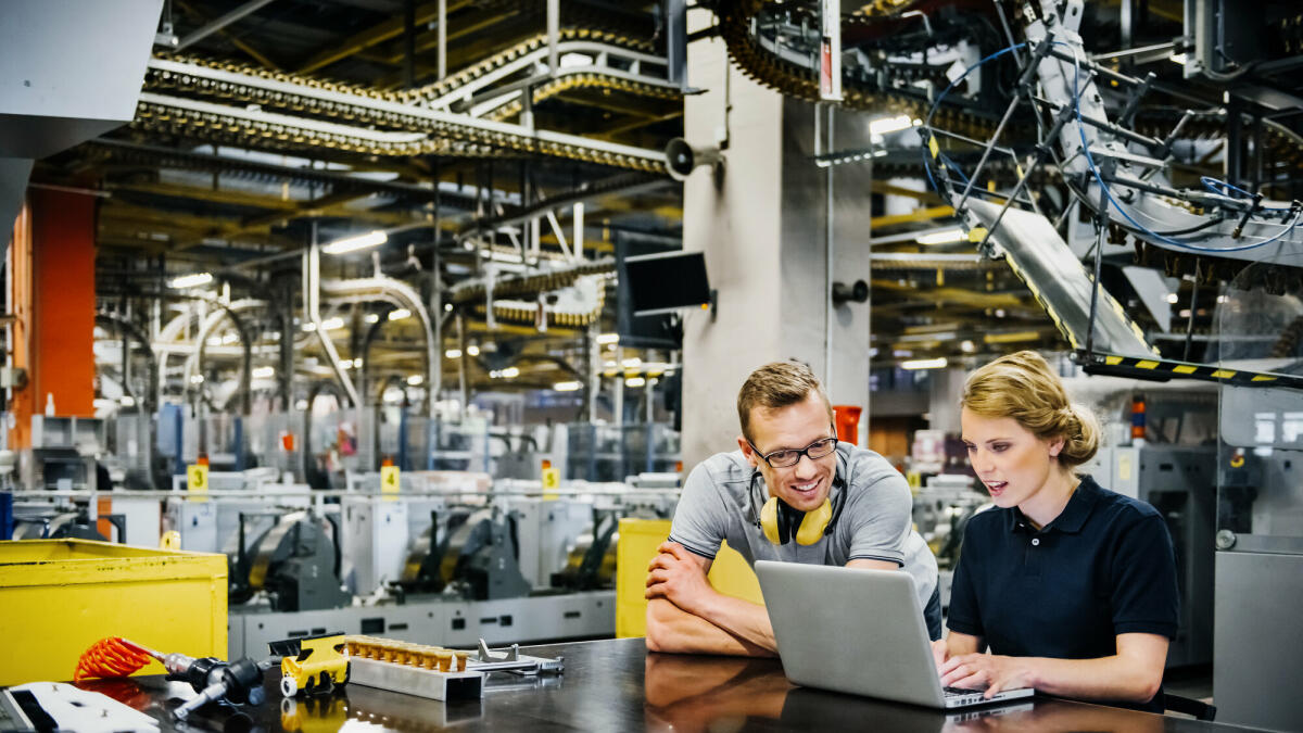 zwei jüngere Ingenieure arbeiten am Laptop in der Verpackungsstraße einer großen Druckerei
 © Tom Werner/ Getty Images