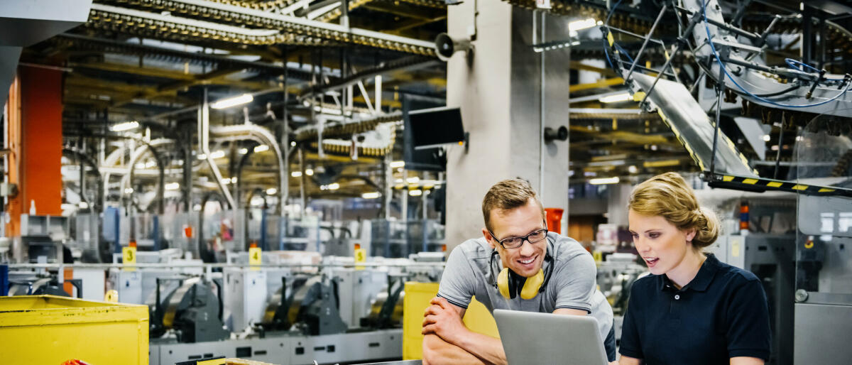 zwei jüngere Ingenieure arbeiten am Laptop in der Verpackungsstraße einer großen Druckerei
 © Tom Werner/ Getty Images