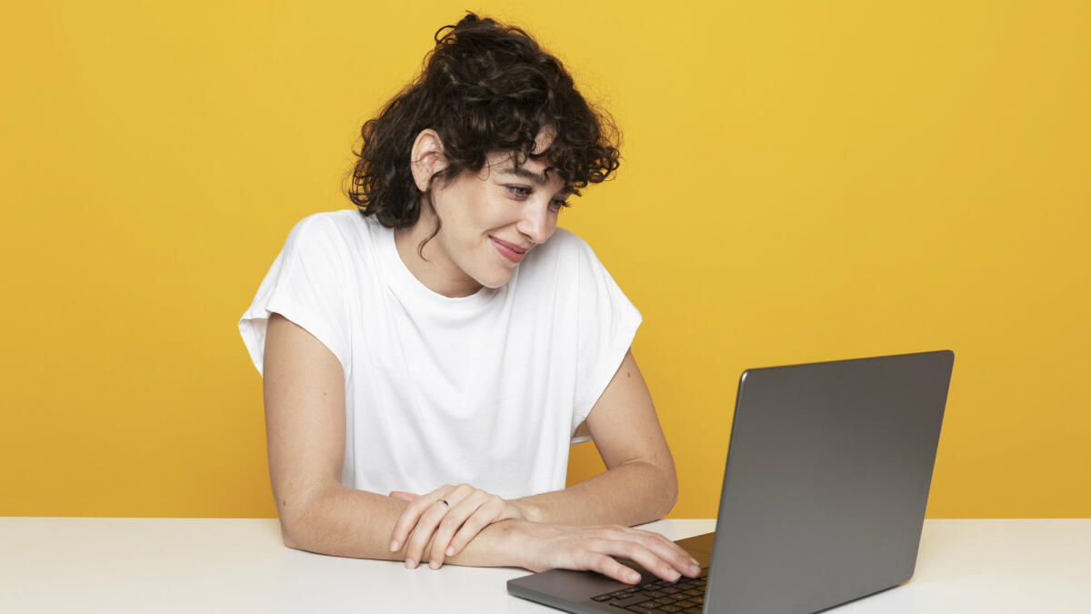 Lächelnde Frau bei der Arbeit am Laptop auf gelbem Hintergrund © Westend61 / Getty Images