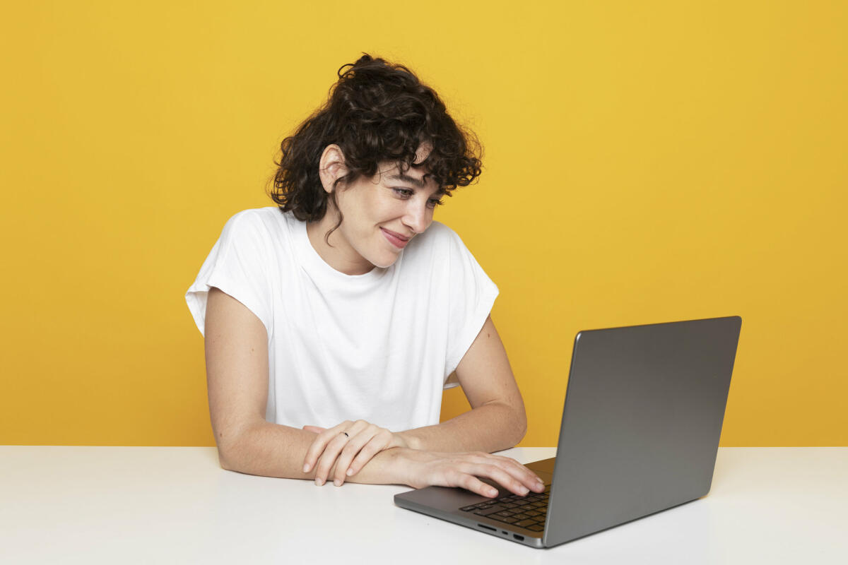 Lächelnde Frau bei der Arbeit am Laptop auf gelbem Hintergrund © Westend61 / Getty Images