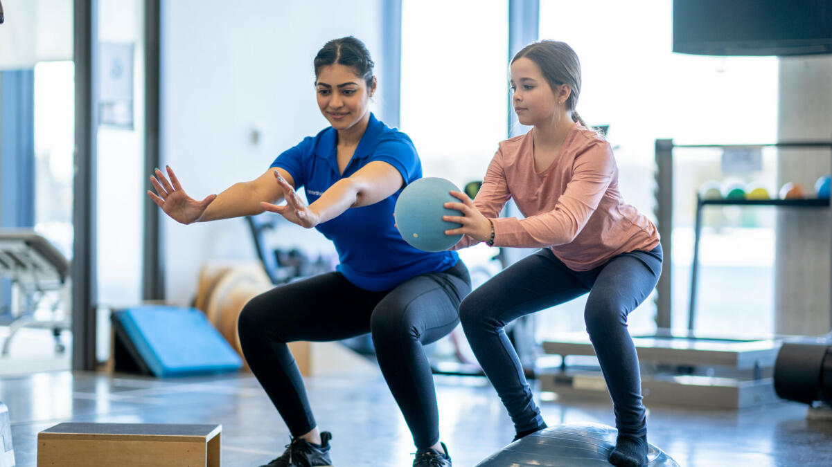 Ein junges Mädchen arbeitet während eines Termins mit ihrem Physiotherapeuten in einer Turnhalle © FatCamera / Getty Images