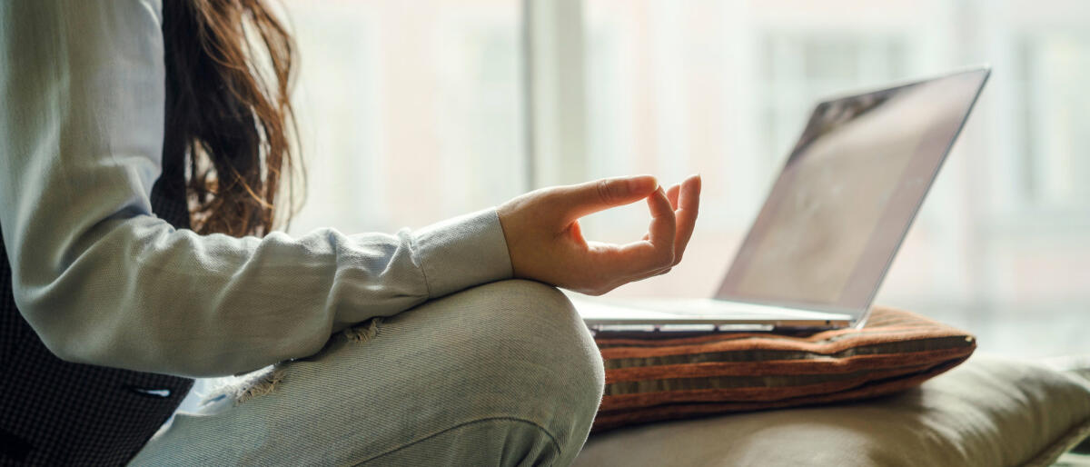 Frau sitzt meditierend vor Laptop. © Fiordaliso / Getty Images