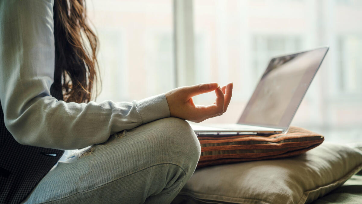 Frau sitzt meditierend vor Laptop. © Fiordaliso / Getty Images