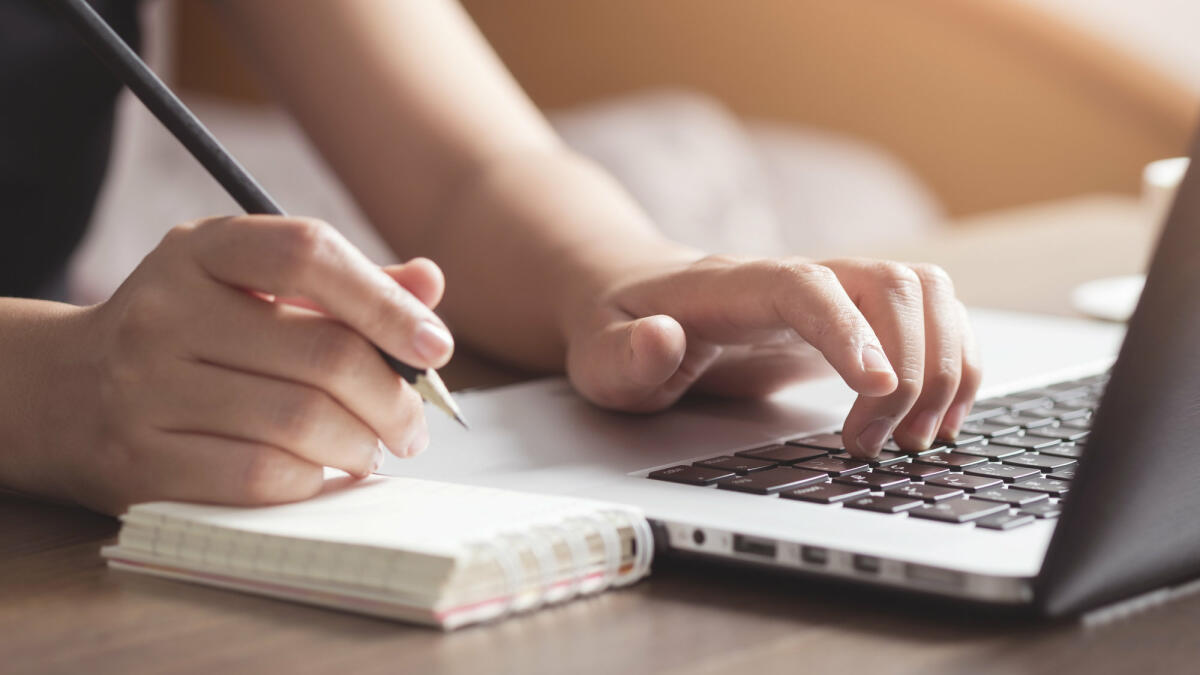 Mensch macht sich Notizen neben einem Laptop. © Twenty47studio / Getty Images