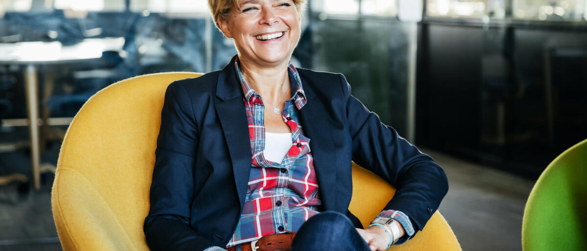 Eine Frau mittleren Alters sitzt lachend in einem gelben Sessel © Tom Werner / Getty Images