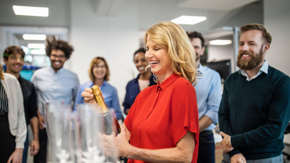 Frau öffnet Sektflasche in Büro © Luis Alvarez / Getty Images