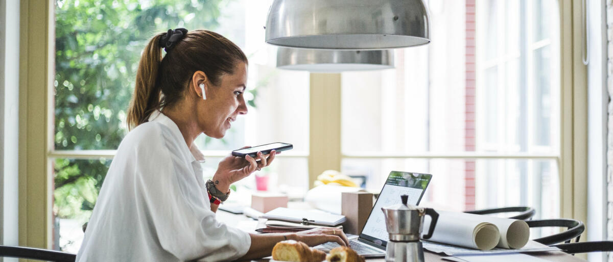 Junge Frau spricht am Schreibtisch in ihr Handy © Maskot / Getty Images