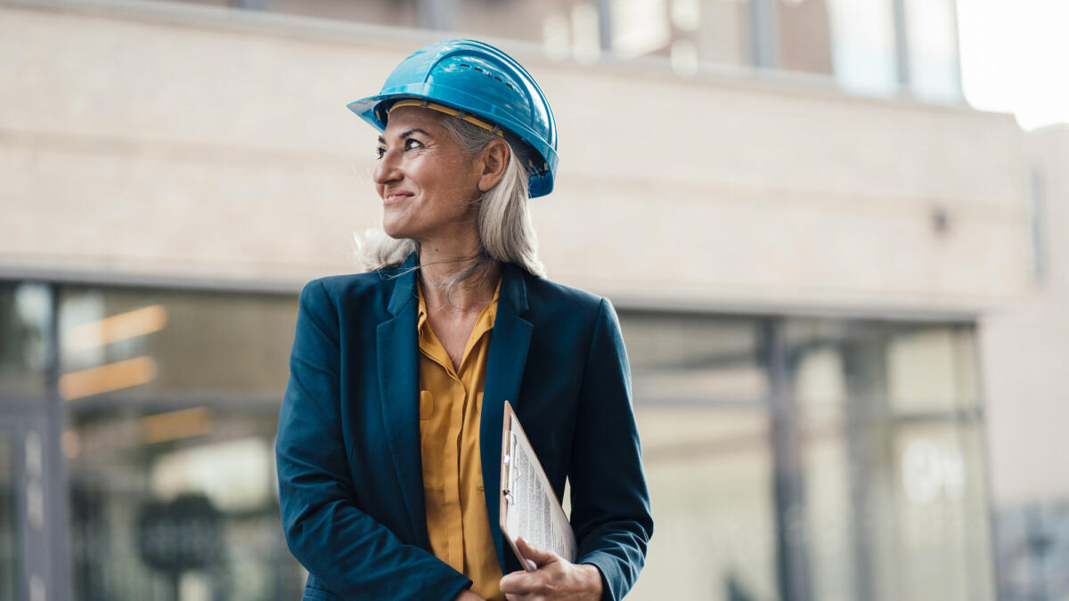 Reife Ingenieurin steht auf einer Baustelle und lächelt © Westend61 / Getty Images