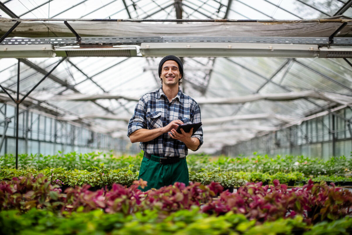 Porträt eines jungen erwachsenen männlichen Gartenarbeiters, der ein digitales Tablet im Gewächshaus benutzt. Mann mit einem Tablet-Computer für Informationen ü © Luis Alvarez/ Getty Images