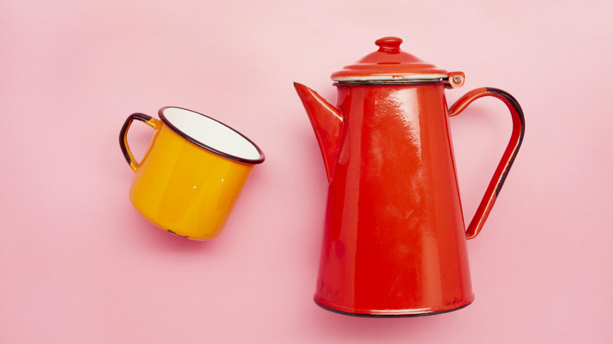 Stilleben einer Emaille-Tasse und einer roten Kaffeekanne auf rosa Hintergrund © the_burtons / Getty Images