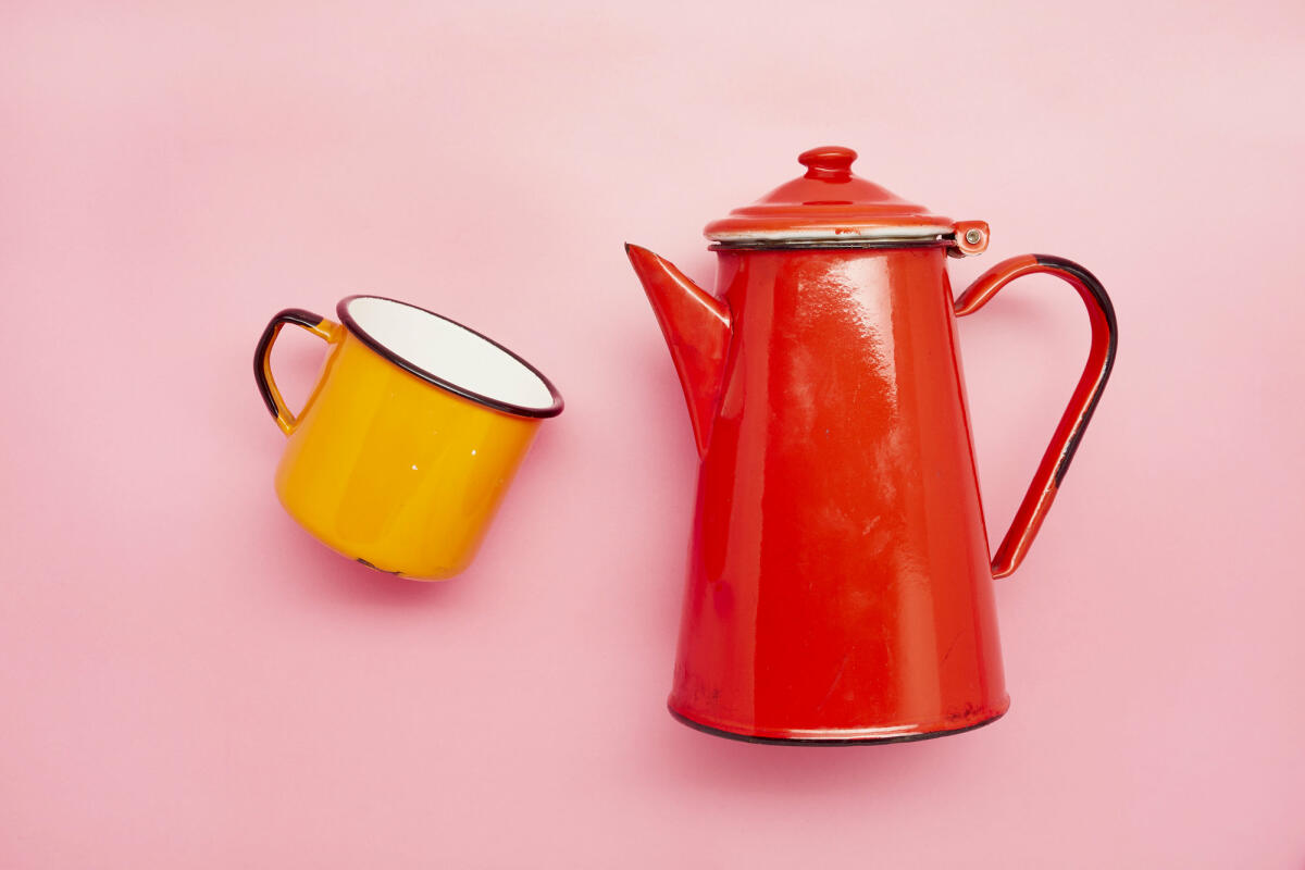 Stilleben einer Emaille-Tasse und einer roten Kaffeekanne auf rosa Hintergrund © the_burtons / Getty Images