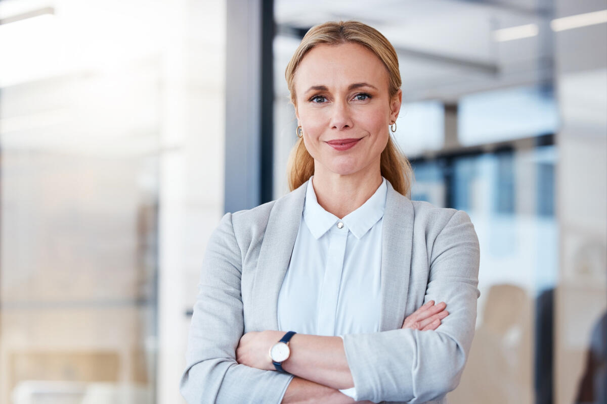 Mittelreife Businessfrau steht selbstbewusst und lächelnd im Raum  © PeopleImages / Getty Images