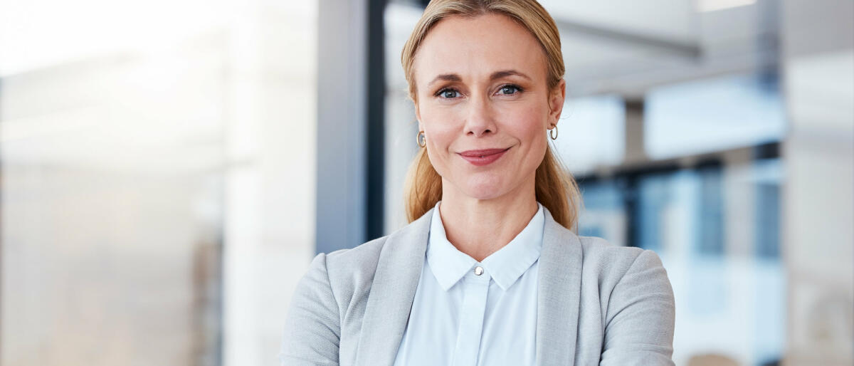 Mittelreife Businessfrau steht selbstbewusst und lächelnd im Raum  © PeopleImages / Getty Images