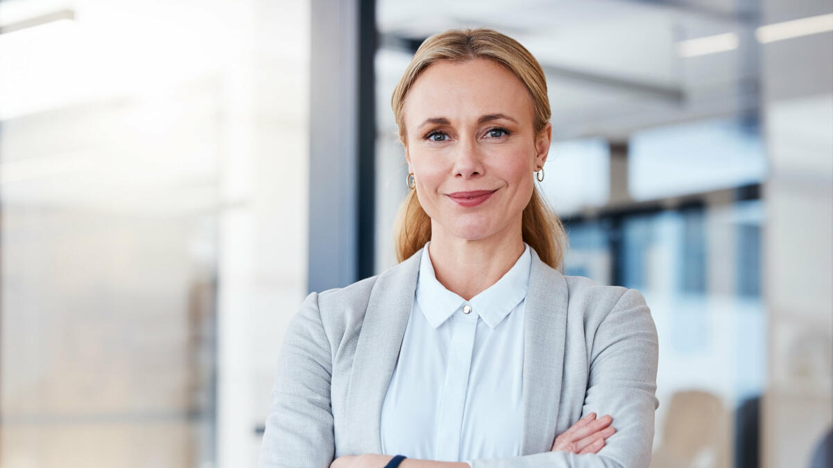 Mittelreife Businessfrau steht selbstbewusst und lächelnd im Raum  © PeopleImages / Getty Images