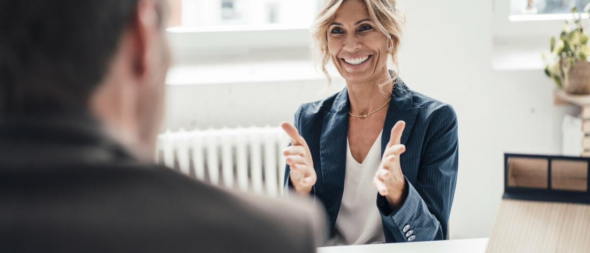 Aufgeregte Bewerberin gestikuliert und spricht mit dem Gegenüber im Büro © Westend61 / Getty Images