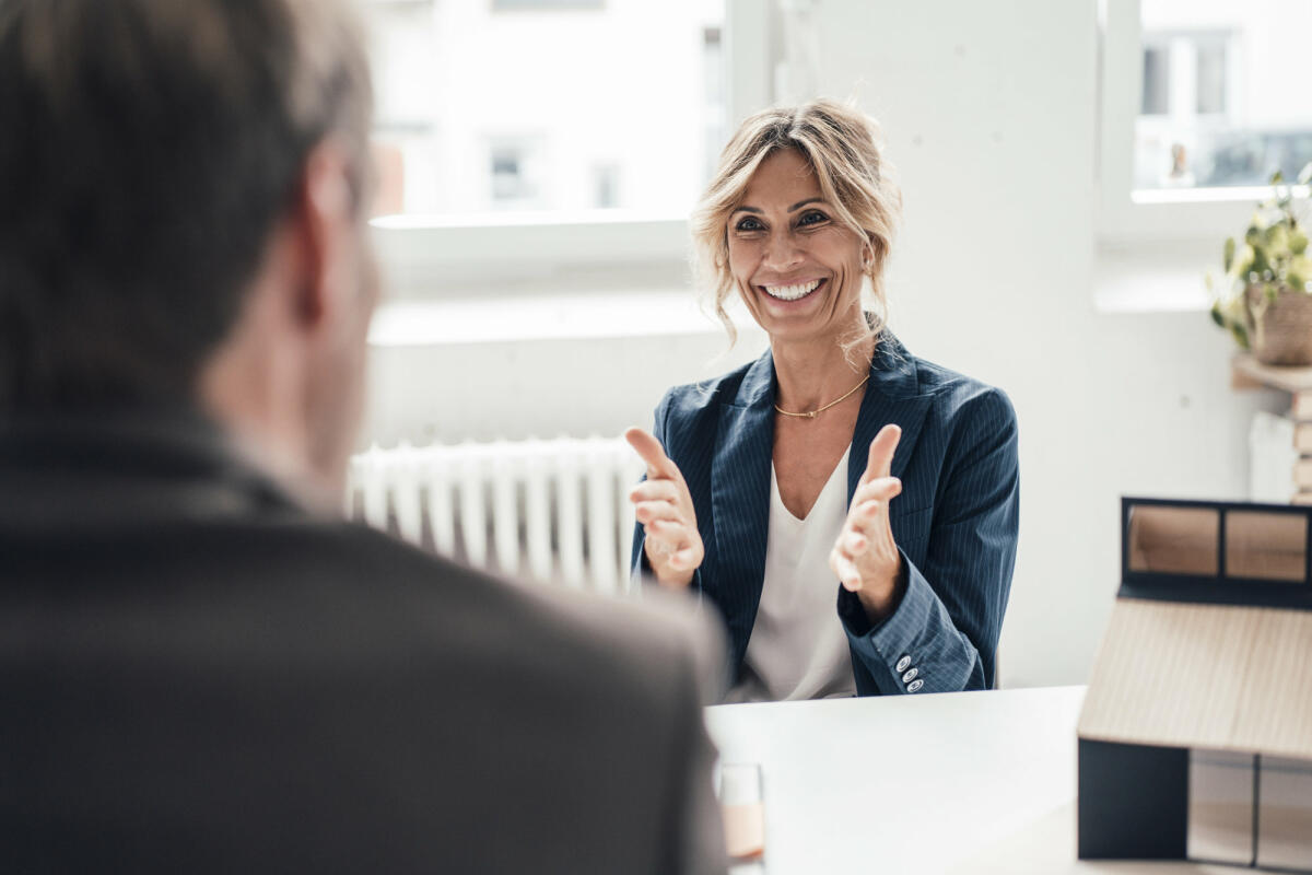 Aufgeregte Bewerberin gestikuliert und spricht mit dem Gegenüber im Büro © Westend61 / Getty Images