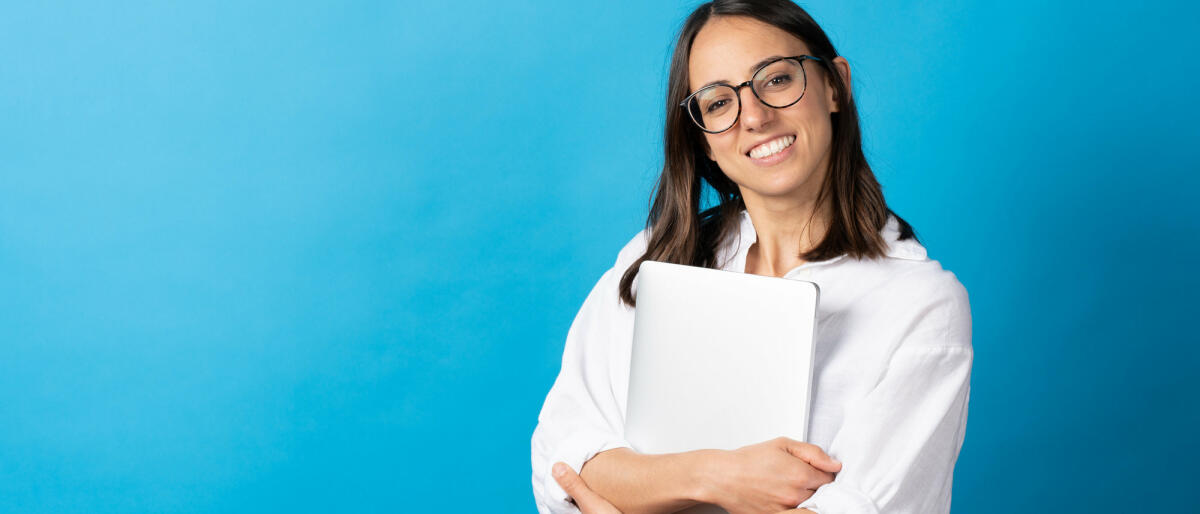 Hübsche hispanische Frau, die einen Laptop hält und in die Kamera schaut © Egoitz Bengoetxea Iguaran / Getty Images