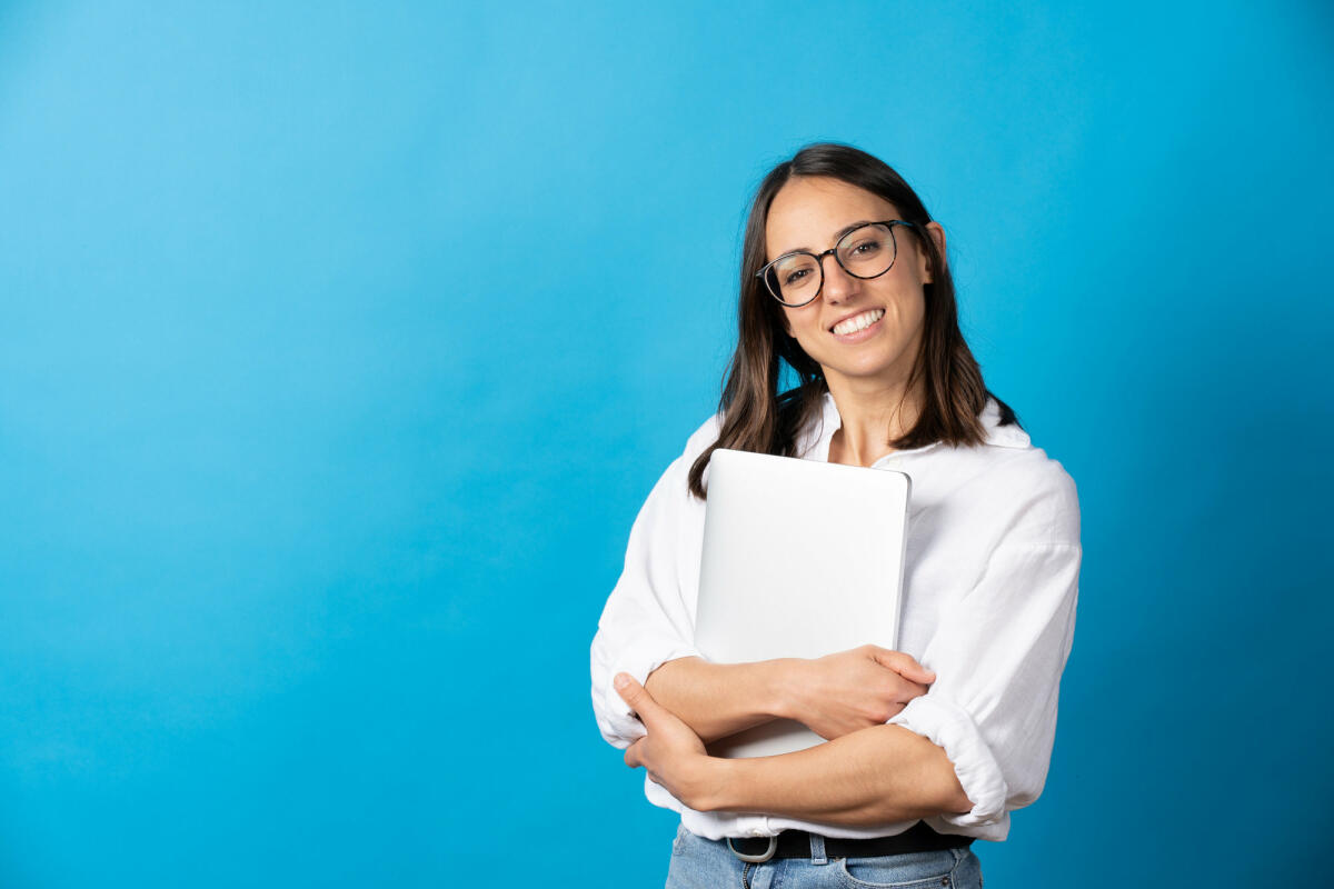 Hübsche hispanische Frau, die einen Laptop hält und in die Kamera schaut © Egoitz Bengoetxea Iguaran / Getty Images