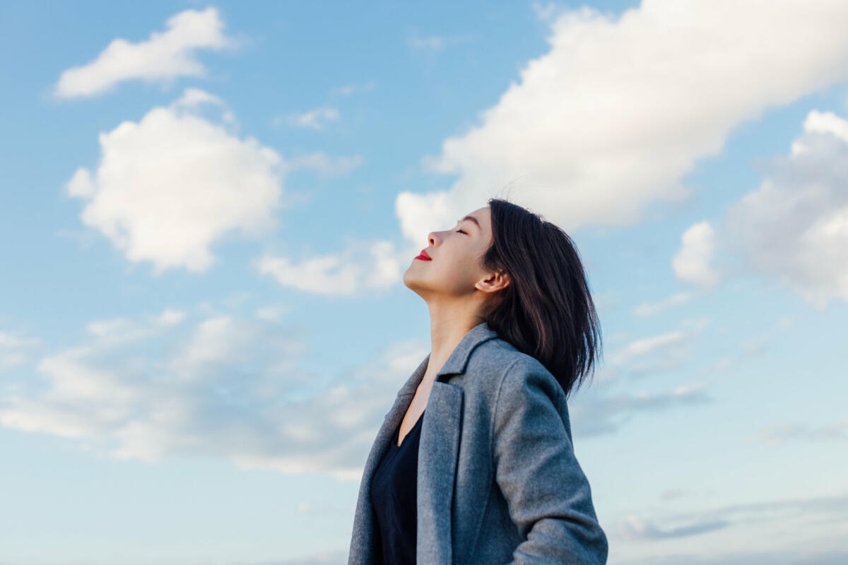 Eine Frau atmet tief ein vor blauem Himmel © Oscar Wong / Getty Images