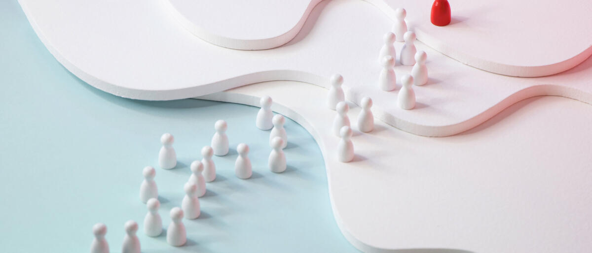 One red figurine leading a row of white figurine on coloured background. © twomeows / getty images