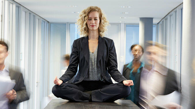 Eine Frau sitzt in Meditations-Position auf deinem Tisch im Büro © Westend61 / Getty Images