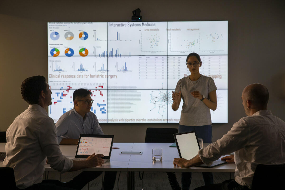 Treffen vor einem großen Informationsgerät zum universellen Nachweis von Genen in einer bestimmten biologischen Probe. © SolStock/ Getty Images