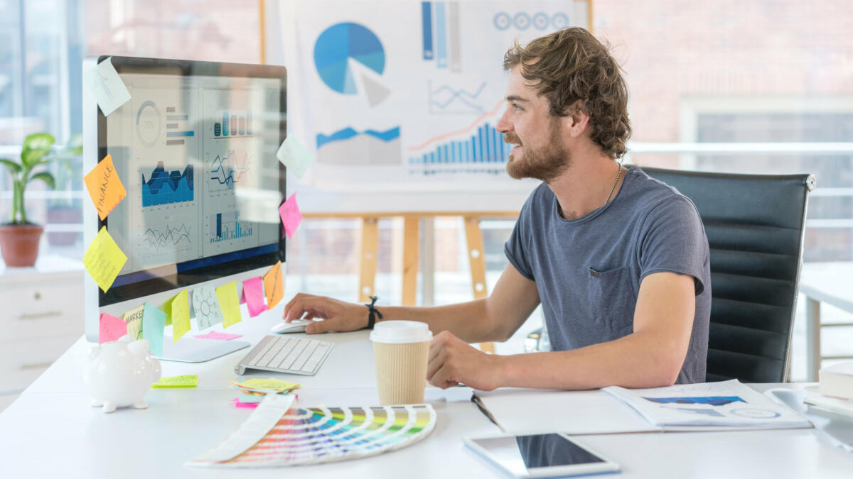 Ein junger Grafikdesigner sitzt vor einem iMac voller Notizzettel © anders / Getty Images