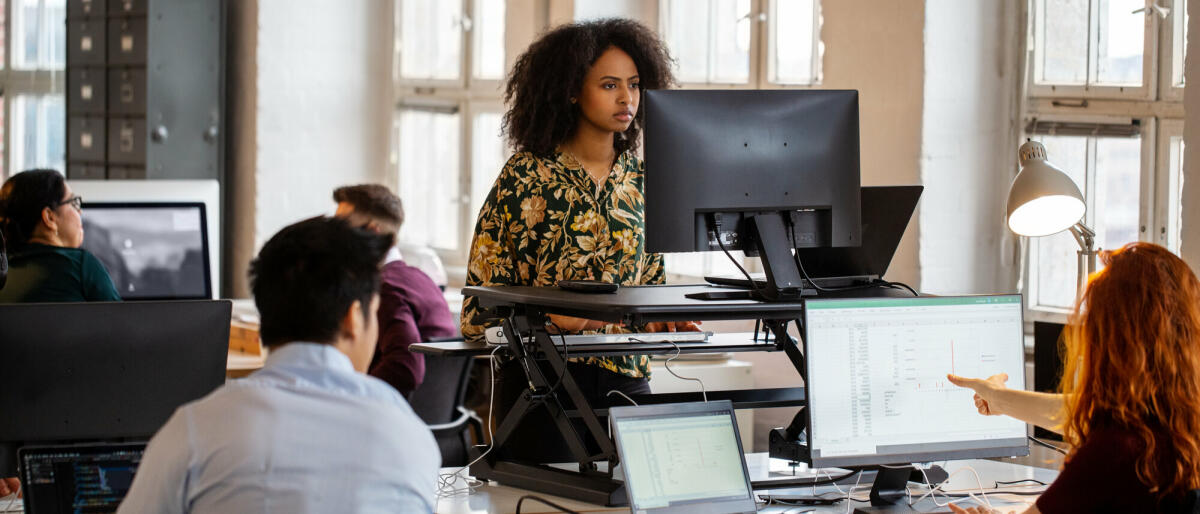 Junge afrikanische Frau arbeitet an einem Stehpult im Büro. Weibliche Mitarbeiterin arbeitet am Computer an einem ergonomischen Stehpult. © Luis Alvarez/ Getty Images