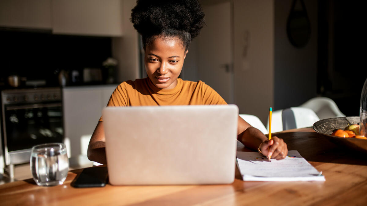 Eine lächelnde Frau sitzt vor ihrem Laptop und schreibt © MStudioImages / Getty Images