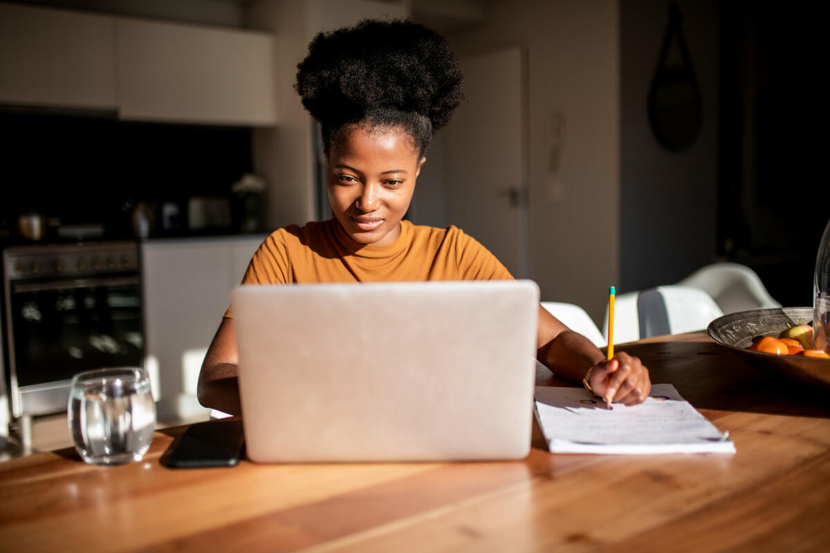 Eine lächelnde Frau sitzt vor ihrem Laptop und schreibt © MStudioImages / Getty Images