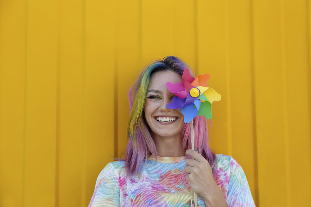 Glückliche Frau trägt Krawatte Farbstoff T-Shirt hält bunte Windrad Spielzeug vor gelben Wand  © Westend61 / Getty Images