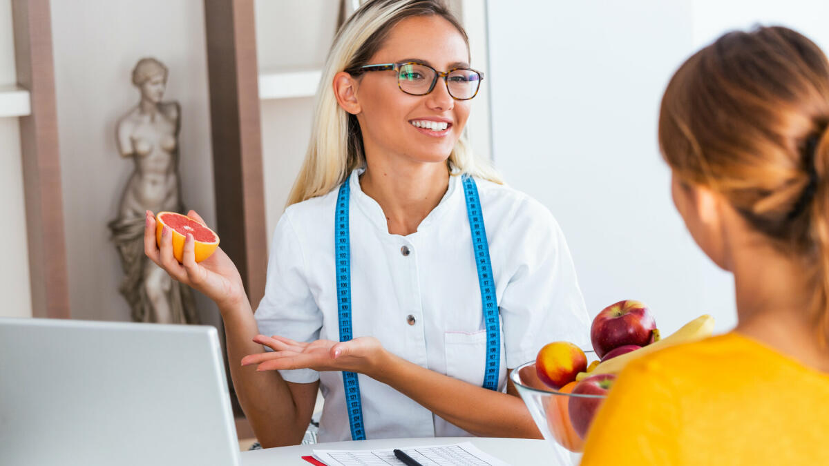 Porträt einer jungen lächelnden Ernährungsberaterin im Sprechzimmer. Diät-Plan. Junge Frau zu Besuch Ernährungsberaterin in Gewichtsverlust Klinik. © stefanamer/ Getty Image