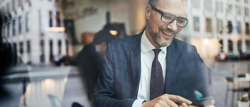 Lachender Mann schaut auf sein Smartphone © Luis Alvarez / Getty Images