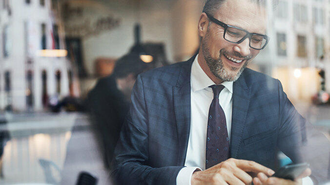 Lachender Mann schaut auf sein Smartphone © Luis Alvarez / Getty Images