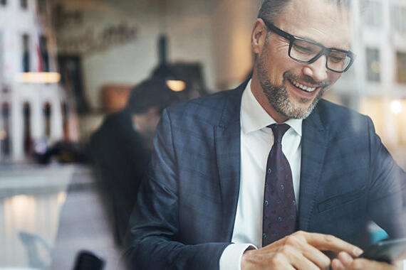 Lachender Mann schaut auf sein Smartphone © Luis Alvarez / Getty Images