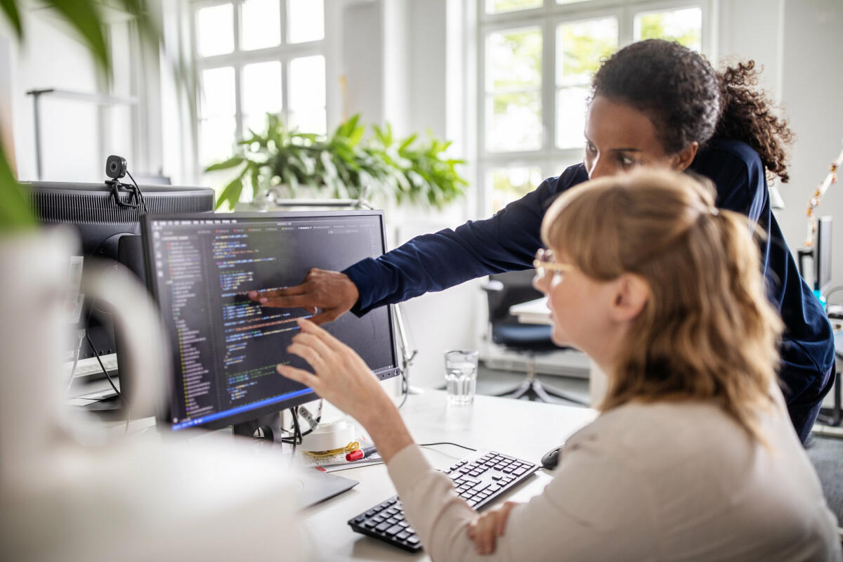 Zwei Frauen gucken auf einen Bildschirm, auf dem Code angezeigt wird © Luis Alvarez / Getty Images