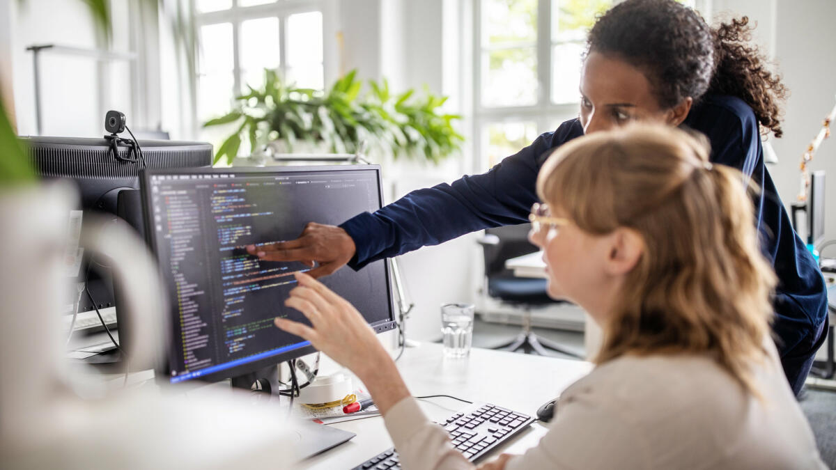 Zwei Frauen gucken auf einen Bildschirm, auf dem Code angezeigt wird © Luis Alvarez / Getty Images