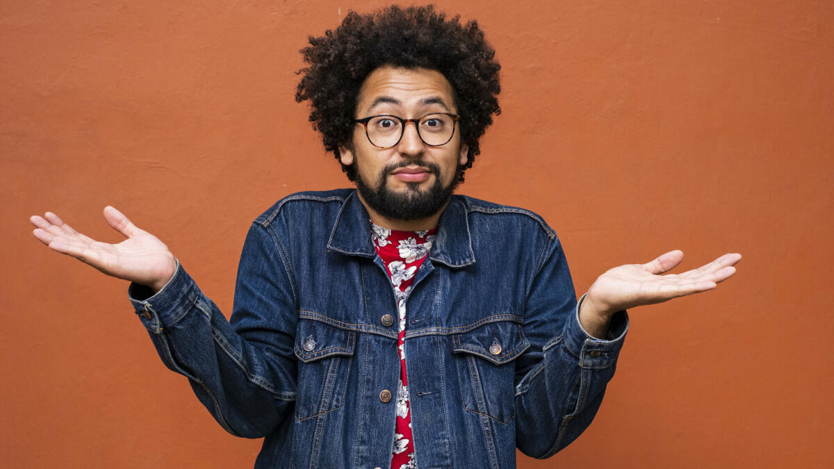 Nicht-binäre Latino-Person mit Brille und Afrofrisur zuckt mit den Schultern und schaut in die Kamera © Sergio Mendoza Hochmann / Getty Images