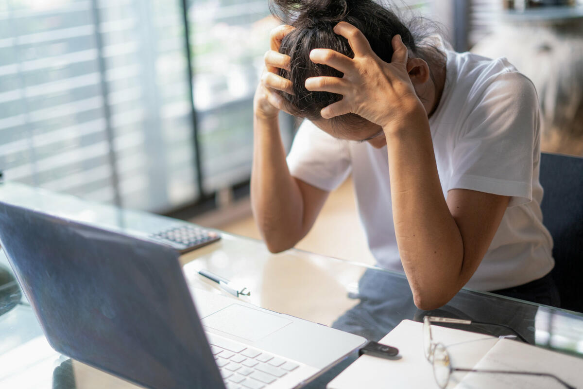 Frau mit Kopfschmerzen sitzt am Laptop © boonchai wedmakawand / Getty Images