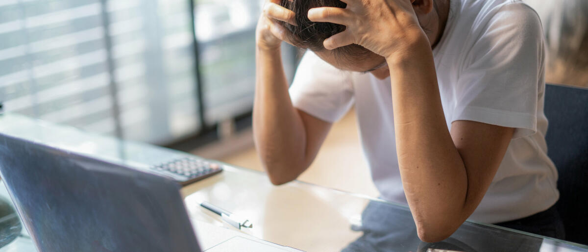 Frau mit Kopfschmerzen sitzt am Laptop © boonchai wedmakawand / Getty Images