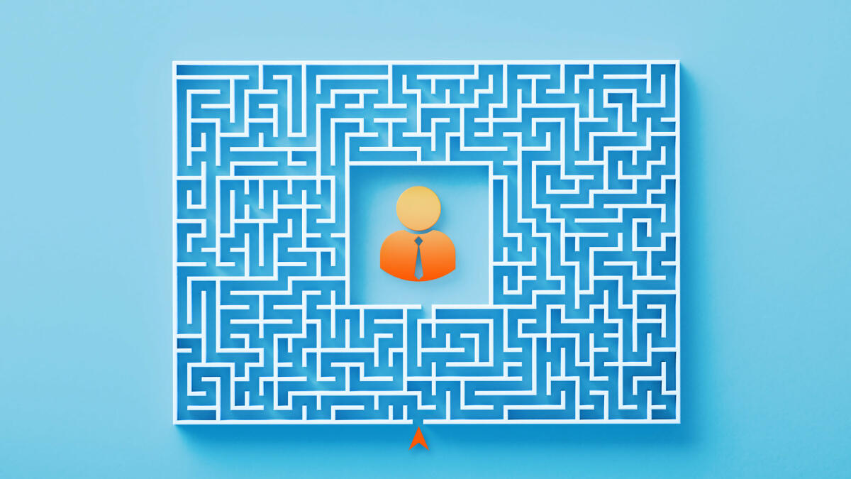 Orangefarbenes Geschäftsmannsymbol, das in der Mitte eines weißen Labyrinths auf blauem Hintergrund sitzt © MicroStockHub / Getty Images