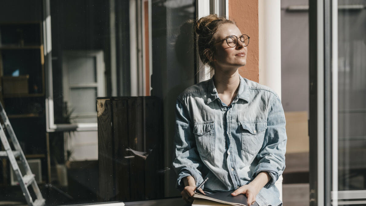 Junge Frau sitzt mit geschlossenen Augen in der Sonne © Westend61 / Getty Images