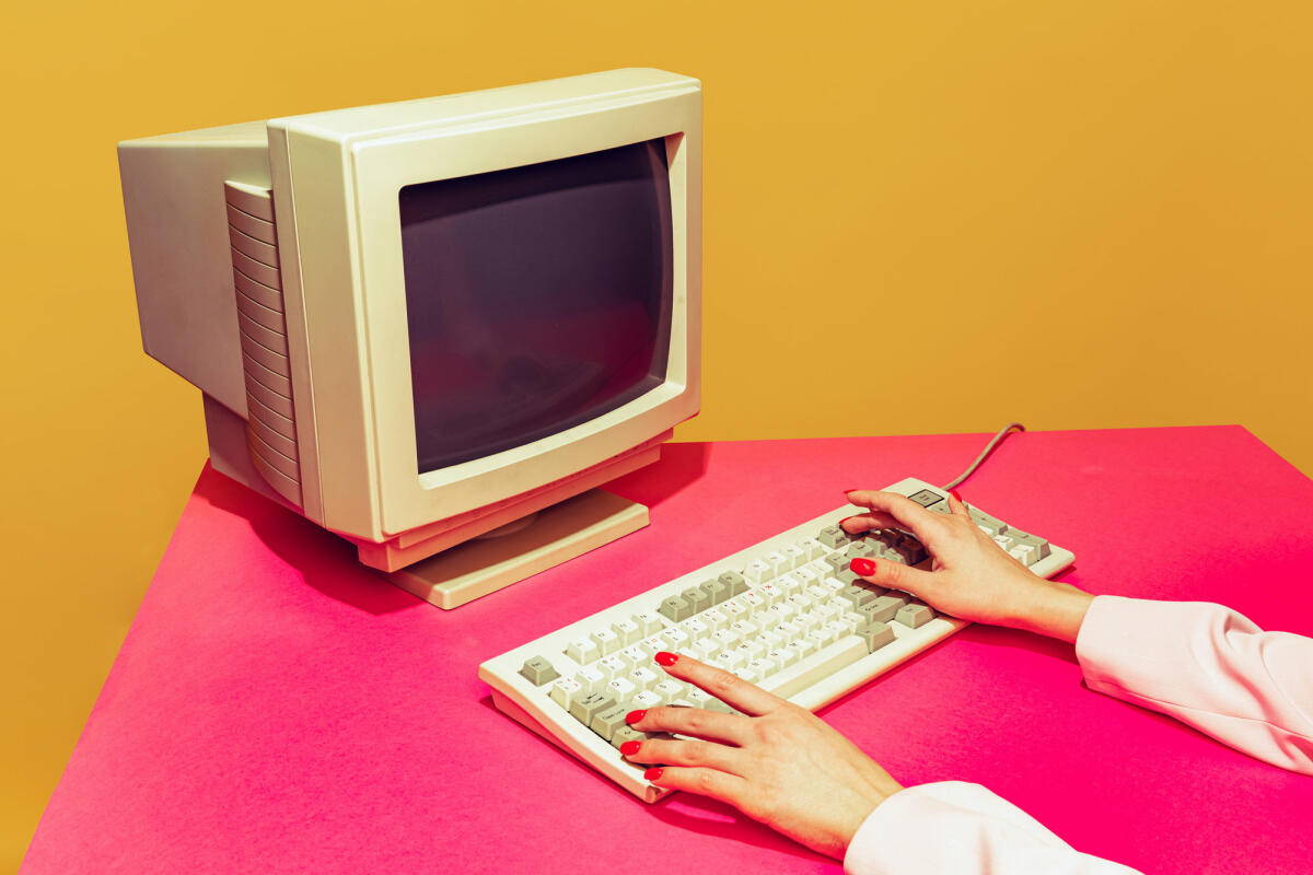 Buntes Bild von Vintage-Computermonitor und Tastatur auf leuchtend rosa Tischdecke über gelbem Hintergrund © master1305 / gettyimages