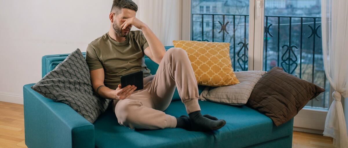 Mann sitzt mit einem Tablet auf dem Sofa und greift sich an den Kopf © Alena Darmel / Pexels