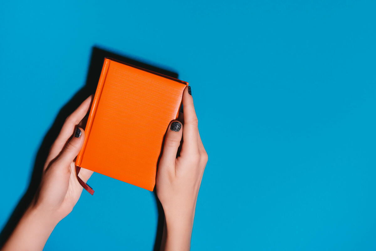 Frau Hände halten orange Tagebuch auf hellen Schreibtisch © Olena Ruban / Getty Images