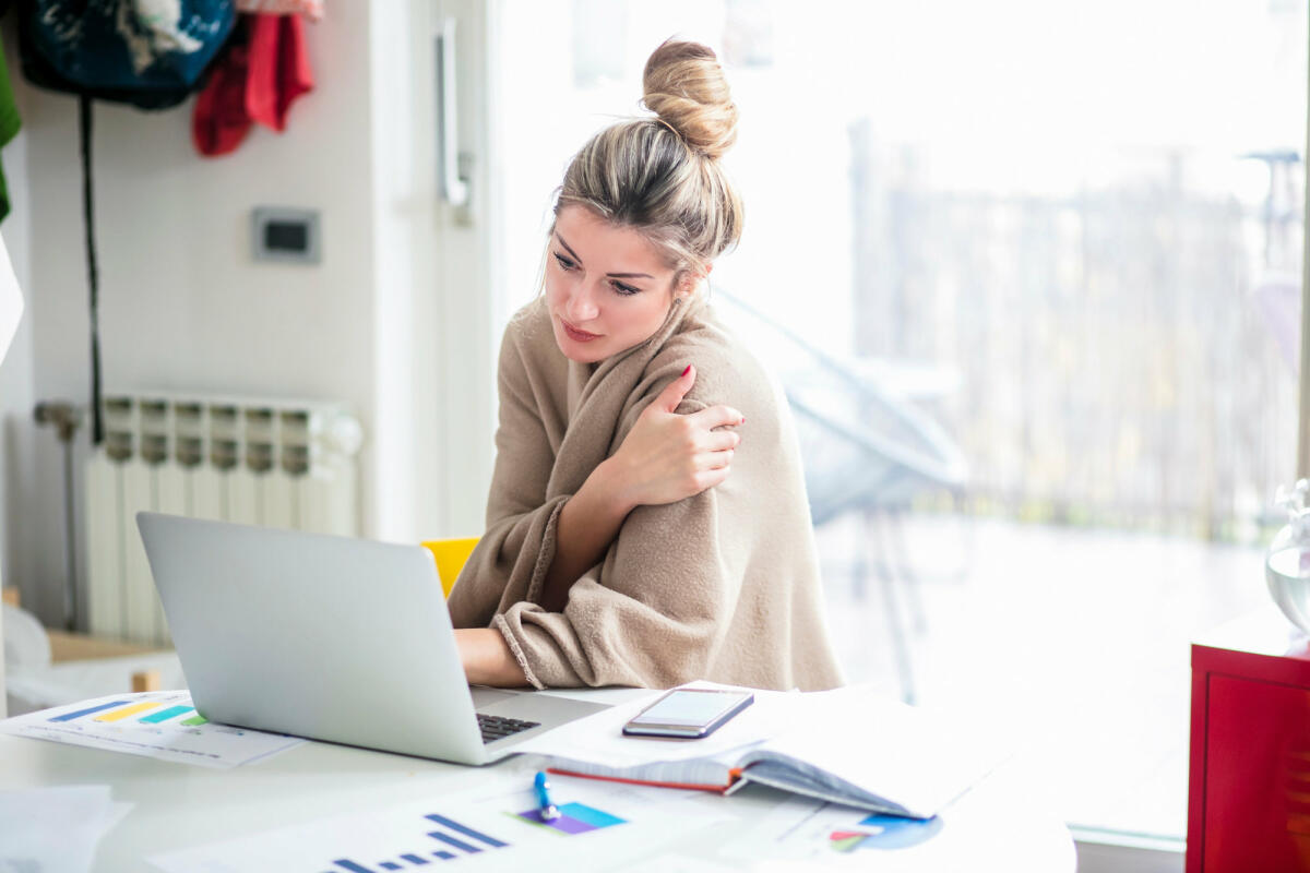 Frau sitzt mit Decke am Schreibtisch © Nikola Ilic / EyeEm / Getty Images