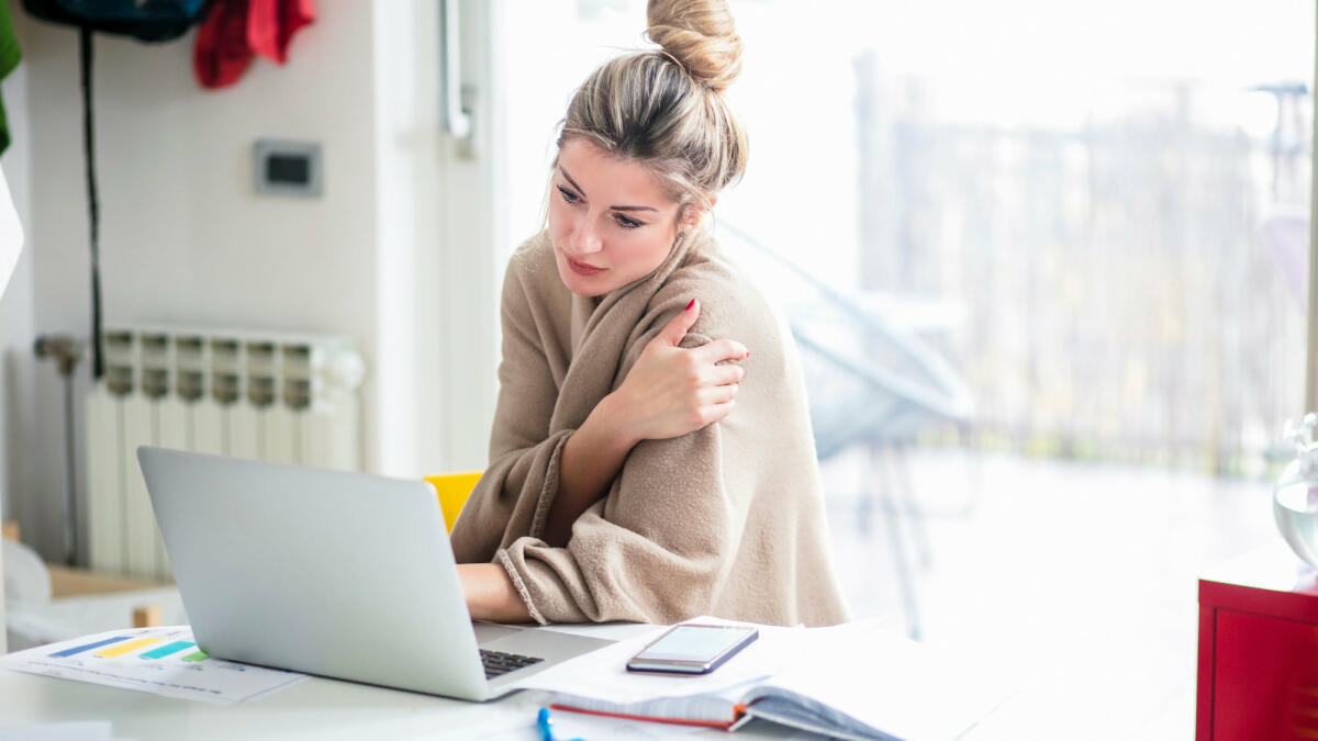 Frau sitzt mit Decke am Schreibtisch © Nikola Ilic / EyeEm / Getty Images