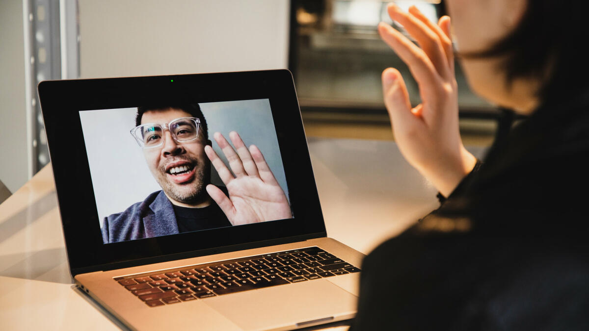 Frau sitzt vor Laptop und winkt Mann in Videokonferenz © Kilito Chan / Getty Images