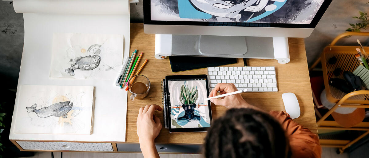 Eine Illustratorin sitzt am Schreibtisch und zeichnet auf ihrem Tablet © Pesic / Getty Images